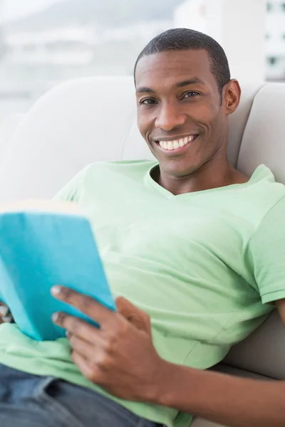 Retrato del hombre afro sonriente leyendo libro en sofá — Foto de Stock