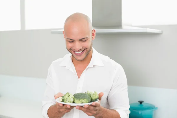 Uomo sorridente con in mano un piatto di broccoli in cucina — Foto Stock