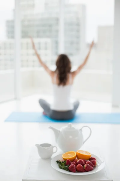 Vrouw zitten in meditatie houding met gezond voedsel op voorgrond — Stockfoto