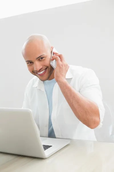 Hombre sonriente casual usando teléfono celular y portátil en el escritorio —  Fotos de Stock