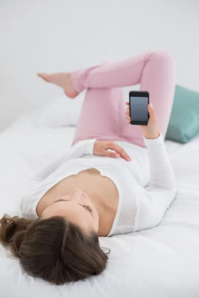 Nyugodt fiatal nő az ágyban a mobiltelefonnal — Stok fotoğraf