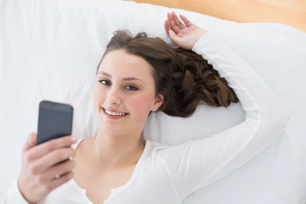 Jonge brunette met mobiele telefoon in bed — Stockfoto