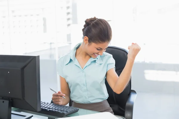 Happy businesswoman clenching fist at office desk — Stock Photo, Image