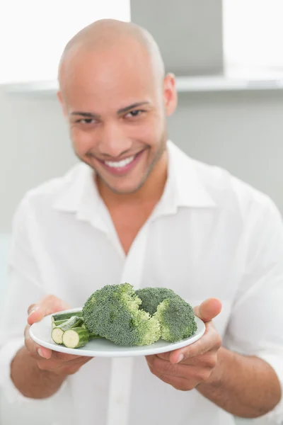 Улыбающийся мужчина держит тарелку брокколи на кухне — стоковое фото