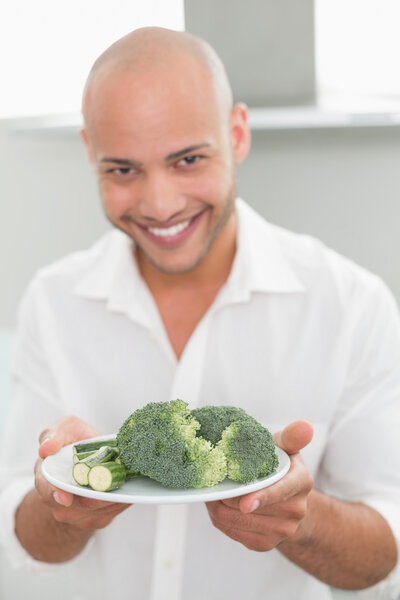 Smiling man holding a plate of broccoli in kitchen