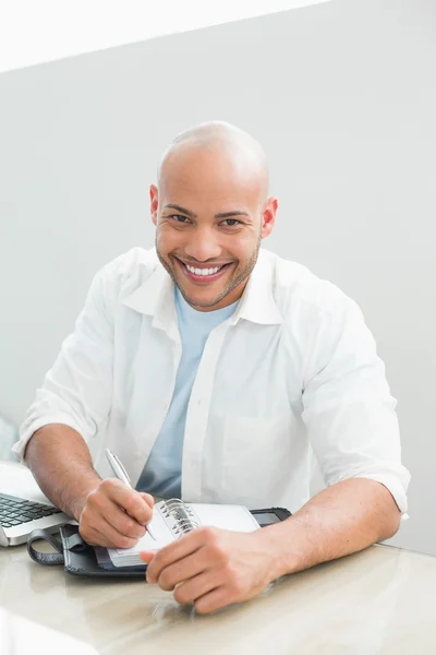 Uomo sorridente casuale con computer portatile che scrive in diario a casa — Foto Stock