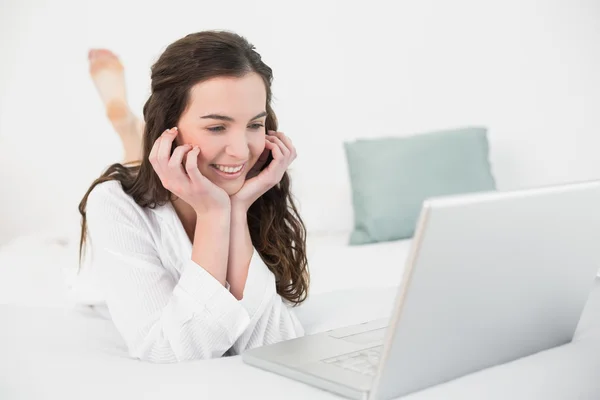 Rilassato bruna casuale utilizzando il computer portatile a letto — Foto Stock