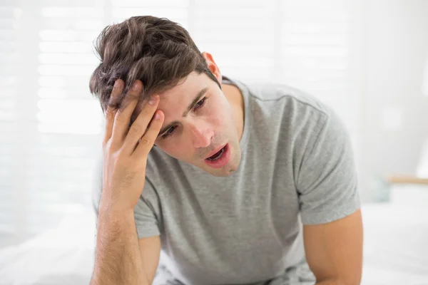 Schläfriger junger Mann sitzt und gähnt im Bett — Stockfoto