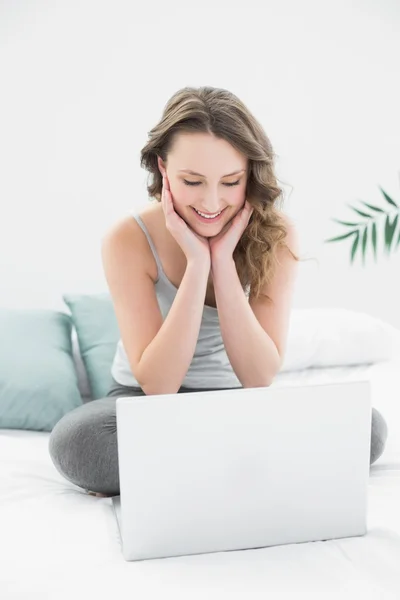 Sonriente morena casual mirando el portátil en la cama —  Fotos de Stock