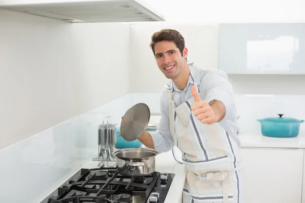 Улыбающийся молодой человек показывает пальцами вверх на кухне — стоковое фото
