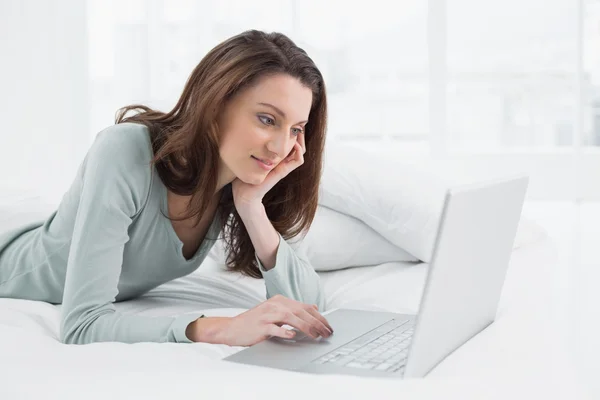 Relajada mujer casual utilizando el ordenador portátil en la cama — Foto de Stock