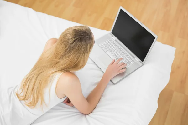Smukła blondynka kobieta za pomocą jej notatnik, leżąc na łóżku — Zdjęcie stockowe