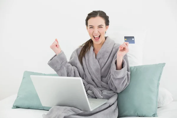 Excited woman in bathrobe doing online shopping in bed — Stock Photo, Image