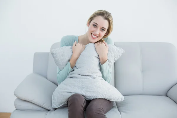 美丽微笑的女人，拥抱着坐在沙发上的枕头 — 图库照片