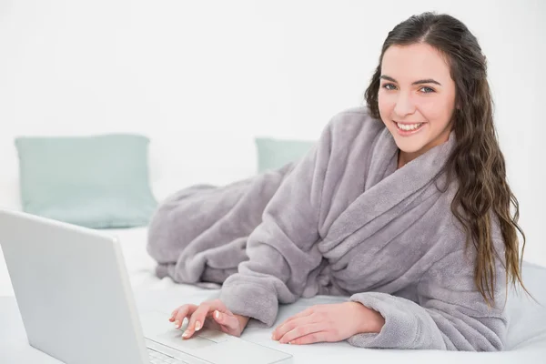 Morena en bata de baño usando laptop en la cama — Stockfoto