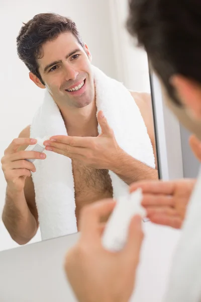 Hombre con reflexión poniendo crema hidratante en la cara —  Fotos de Stock