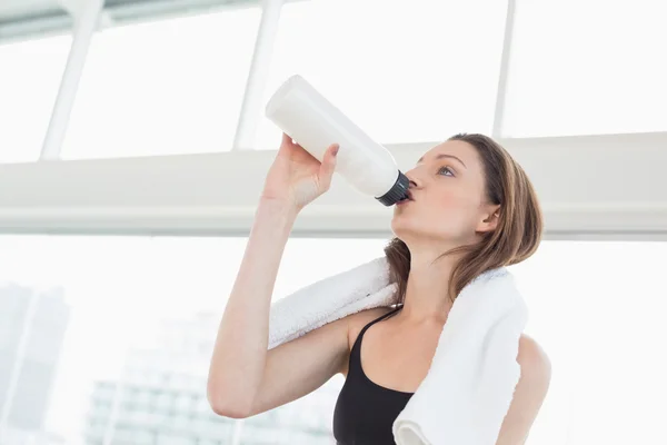 Fit woman with towel around neck drinking water in fitness studio — Stock Photo, Image