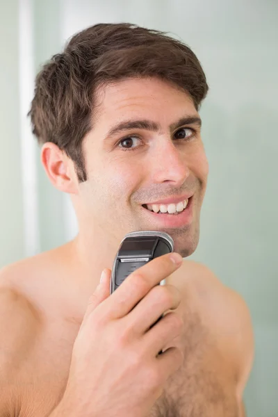 Sonriente hombre guapo sin camisa afeitándose con afeitadora eléctrica — Foto de Stock