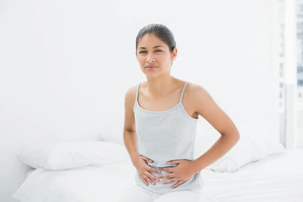 Mujer casual con dolor de estómago sentada en la cama — Foto de Stock