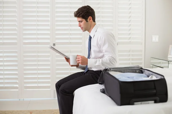 Businessman with coffee cup and newspaper by luggage at hotel room — Stock Photo, Image