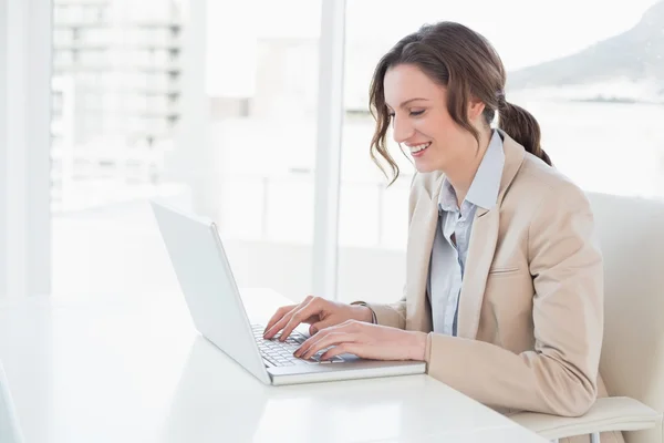 Lachende jonge zakenvrouw met behulp van laptop op kantoor — Stockfoto