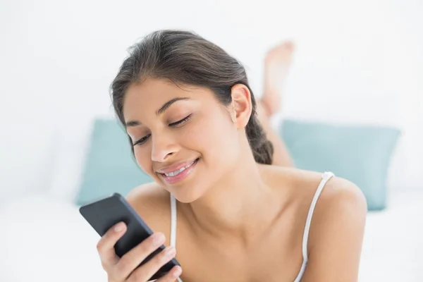 Lächelnde Frau blickt auf Handy im Bett — Stockfoto