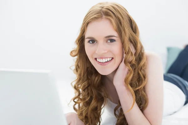 Portret van een glimlachende roodharige meisje met laptop in bed — Stockfoto
