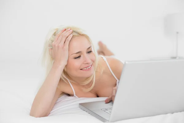 Avslappnad avslappnad blond med laptop i sängen — Stockfoto