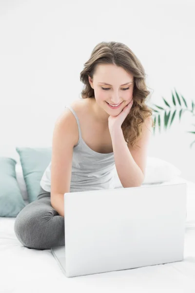 Sonriente morena casual mirando el portátil en la cama — Foto de Stock