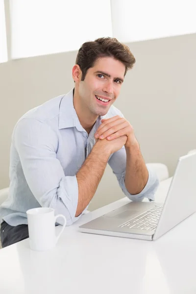 Uomo sorridente casuale che utilizza il computer portatile a casa — Foto Stock