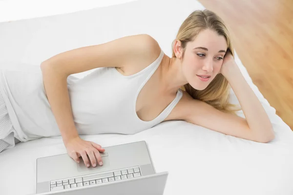 Thoughtful calm woman using her notebook lying on her bed — Stock Photo, Image