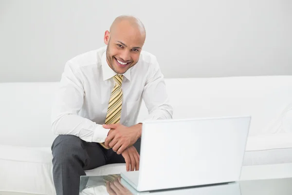 Empresário sorrindo usando laptop no sofá em casa — Fotografia de Stock