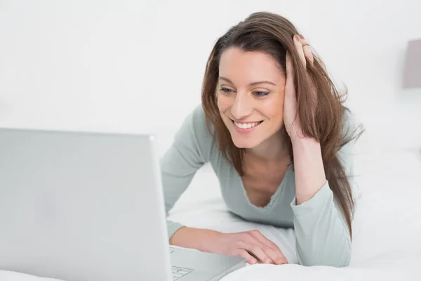 Relajada mujer sonriente casual utilizando el ordenador portátil en la cama —  Fotos de Stock