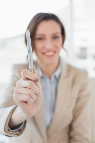Smiling businesswoman holding out a pen in office — Stock Photo, Image