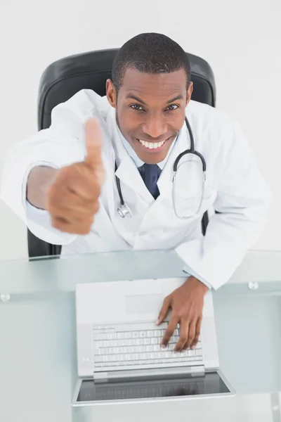 Sorridente medico maschio con il computer portatile gesticolando pollici verso l'alto — Foto Stock