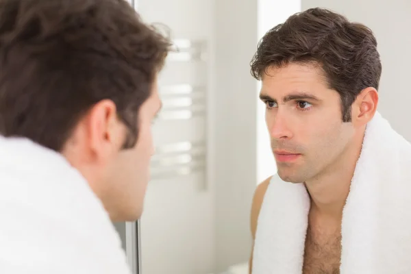 Serious young man looking at self in bathroom mirror — Stock Photo, Image