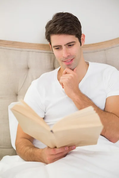 Entspannter junger Mann liest Buch im Bett — Stockfoto