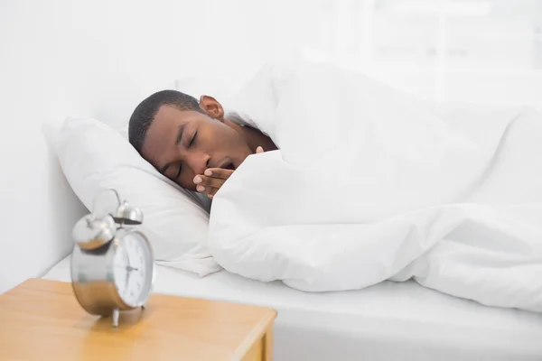 Afro-Mann gähnt im Bett mit Wecker im Vordergrund — Stockfoto