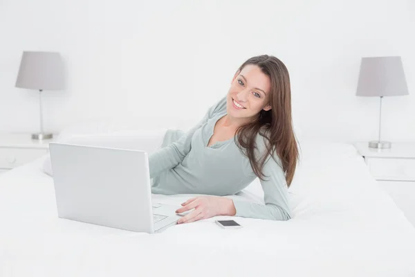 Relajada mujer joven casual utilizando el ordenador portátil en la cama — Foto de Stock