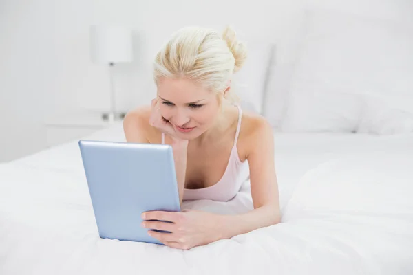 Innehåll casual ung blond med hjälp av TabletPC i sängen — Stockfoto