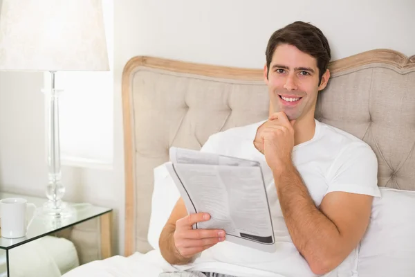 Casual man reading newspaper in bed — Stock Photo, Image