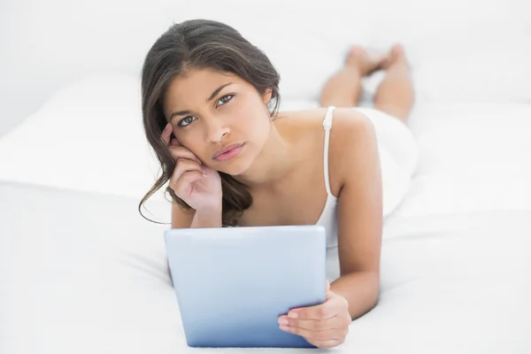 Thoughtful casual woman using tablet PC in bed — Stock Photo, Image