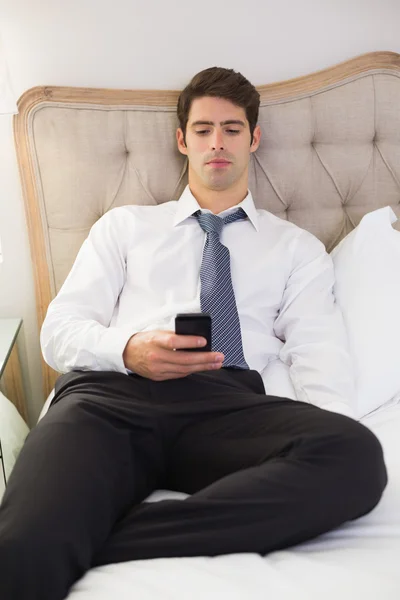 Ernstige goed geklede man van het tekstoverseinen in bed — Stockfoto
