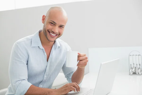 Hombre casual usando el ordenador portátil mientras bebe café en casa — Foto de Stock