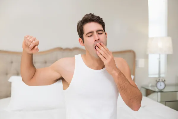 Jovem acordando na cama e esticando os braços — Fotografia de Stock