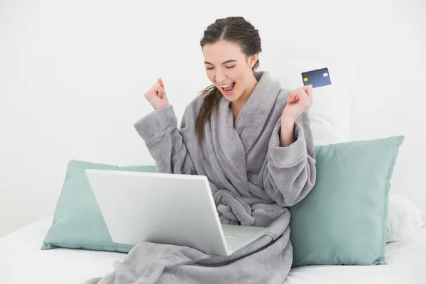 Excited woman in bathrobe doing online shopping in bed — Stock Photo, Image