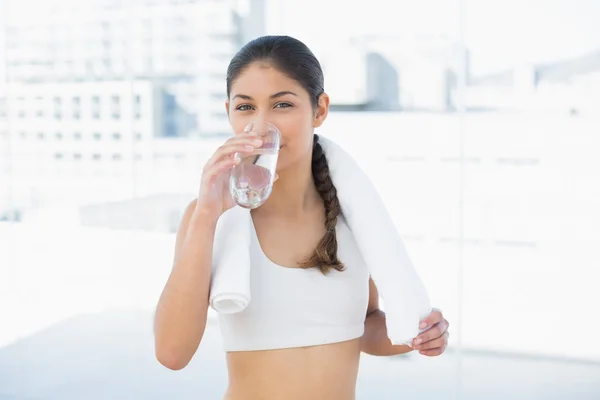 Woman with towel around neck drinking water in fitness studio — Stock Photo, Image