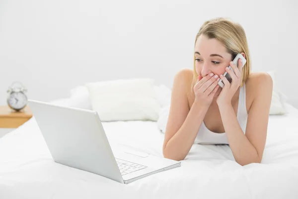 Beautiful woman phoning while lying on her bed using her notebook — Stock Photo, Image