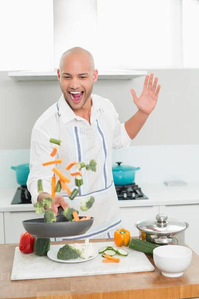 Cheerful man tossing vegetables in the kitchen — Stock Photo, Image