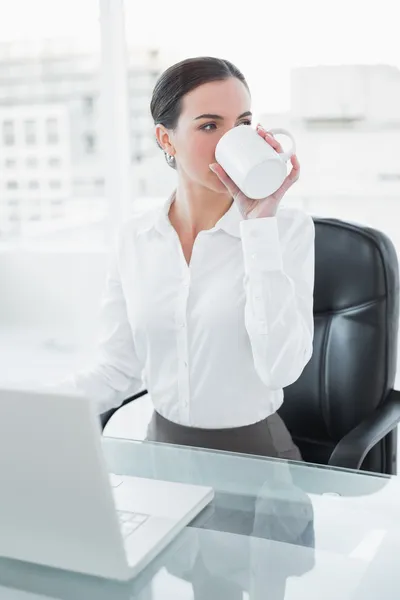 Empresaria bebiendo café mientras usa el portátil en el escritorio —  Fotos de Stock